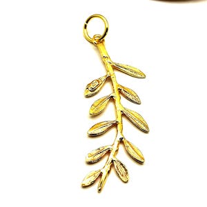 May include: A gold-colored pendant in the shape of an olive branch with leaves. The pendant is on a white background.