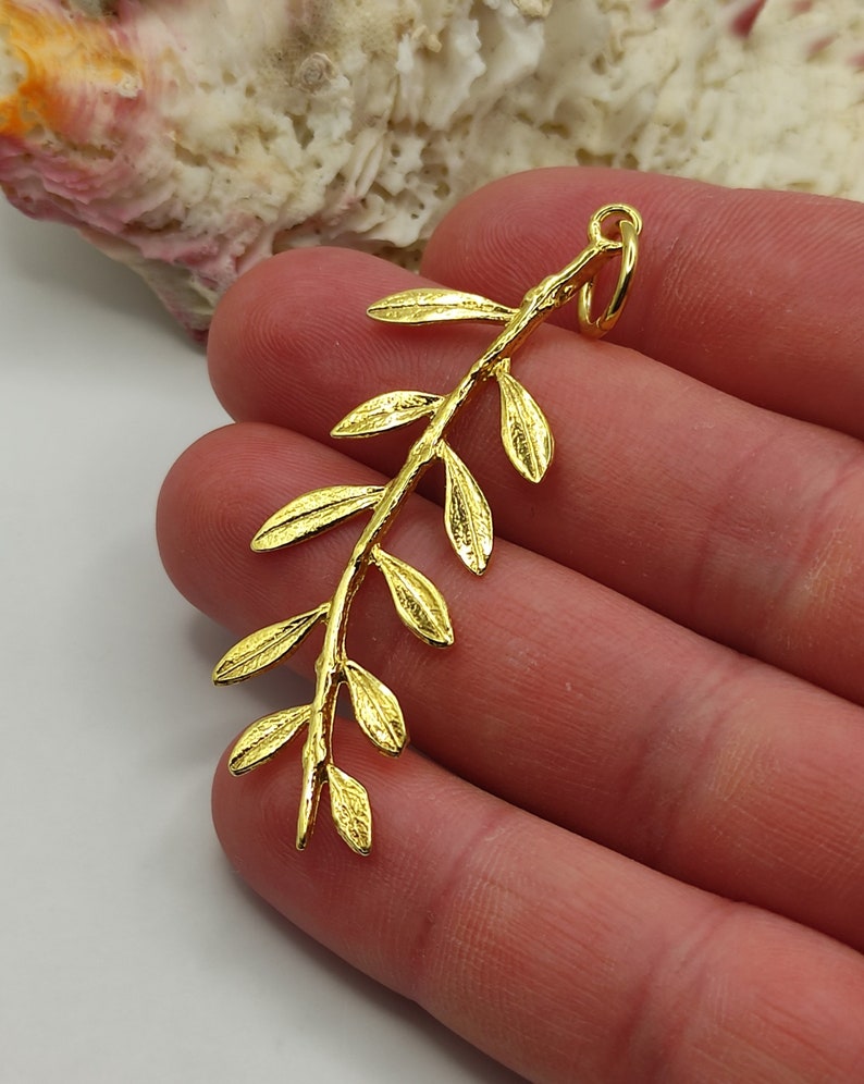 May include: Gold-toned metal pendant shaped like an olive branch with multiple leaves.