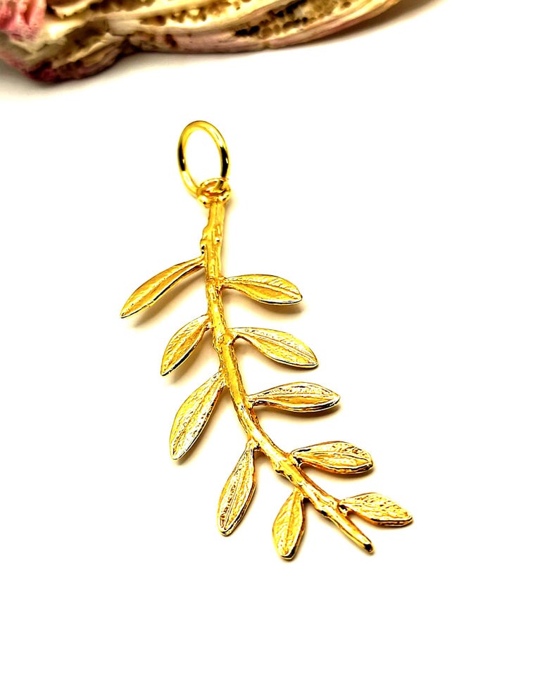 May include: A gold-colored olive branch pendant with a textured finish. The pendant features a delicate stem with multiple leaves.