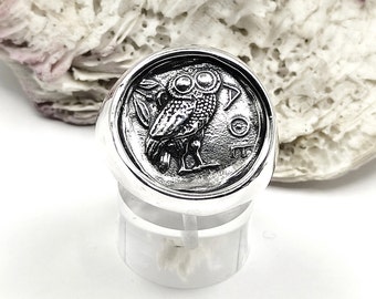 May include: A silver ring with an owl design. The owl is facing forward with its wings spread out. The ring is set on a white background.