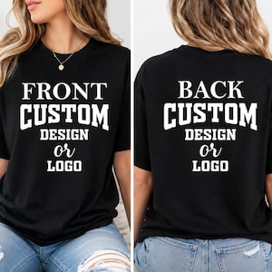 May include: Black t-shirt with white text on the front: "FRONT CUSTOM DESIGN OR LOGO." The back of the shirt has the text "BACK CUSTOM DESIGN OR LOGO." The shirt is worn with blue jeans.