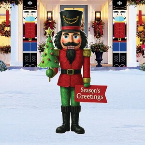 May include: A large, outdoor Christmas nutcracker statue, holding a green Christmas tree and a sign that reads "Season's Greetings." The nutcracker wears a red coat, green pants, and a black hat. Two matching nutcracker banners flank the entrance.