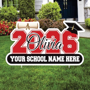 May include: A red and white graduation yard sign with the year "2026" and the name "Olivia" in a script font. The sign includes a graduation cap, a diploma, and space for a school name.