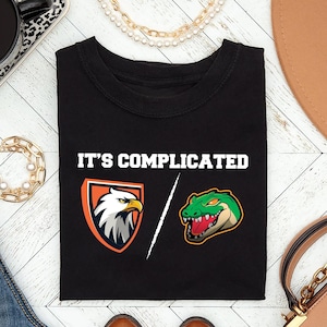May include: Black t-shirt with the text "It's complicated" and a graphic of an eagle and an alligator.