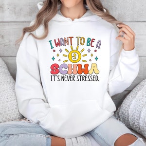 May include: White hooded sweatshirt with the text "I want to be a schwa it's never stressed." in colorful letters with a sun and stars graphic.