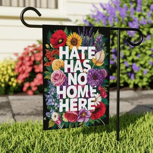 May include: A black garden flag with a floral design and the text "Hate Has No Home Here".