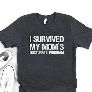 May include: A dark gray t-shirt with the text "I survived my mom's doctorate program" in white.