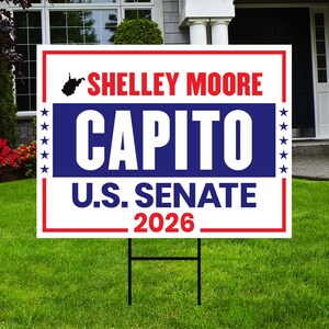 May include: A white and red political yard sign with the text "Shelley Moore Capito U.S. Senate 2026" in red and blue. The sign is displayed on a green lawn with a black metal stake.