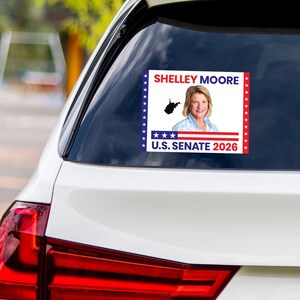 May include: A rectangular sticker on a car window displays a portrait of Shelley Moore, the text "SHELLEY MOORE," and "U.S. SENATE 2026." The sticker has a blue and red border with stars and a West Virginia outline.