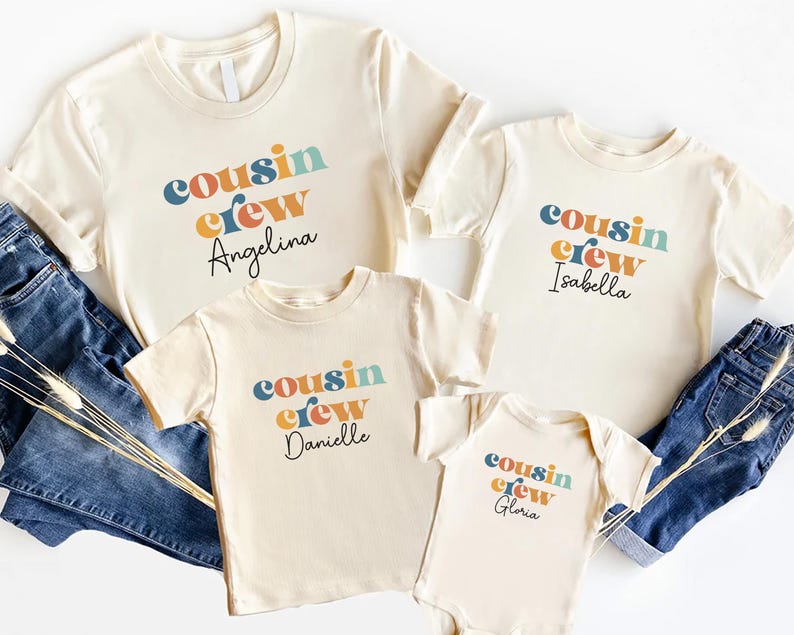 May include: Four beige t-shirts with the text "cousin crew" in colorful letters and a name underneath. The names are Angelina, Isabella, Danielle, and Gloria.