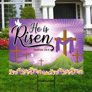 May include: Purple and green Easter yard sign with the text "He is Risen" and the Bible verse Matthew 28:6. The sign features a white dove, three crosses, and a purple cloth draped over the center cross.