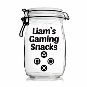 Peut inclure: Un pot en verre transparent avec un couvercle noir et une &eacute;tiquette qui dit "Liam's Gaming Snacks". L'&eacute;tiquette comporte &eacute;galement quatre symboles de manette noirs&nbsp;: un carr&eacute;, un cercle, un X et un triangle.