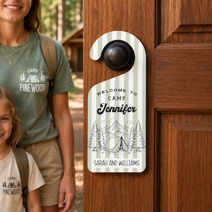 May include: A vertical door hanger with a light green and white striped pattern. The text reads Welcome to Camp Jennifer and Sarah and Williams. A black line art illustration features a tent surrounded by pine trees and mountain peaks.