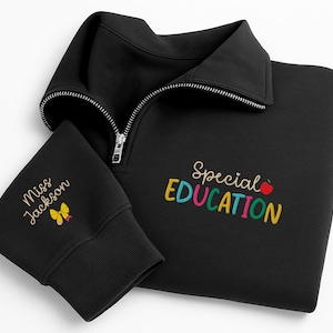 May include: Black sweatshirt with a quarter-zip collar. The sleeve cuff features the embroidered text "Miss Jackson" and a yellow butterfly. The front of the sweatshirt displays the words "Special Education" in colorful embroidery, with a red apple graphic.