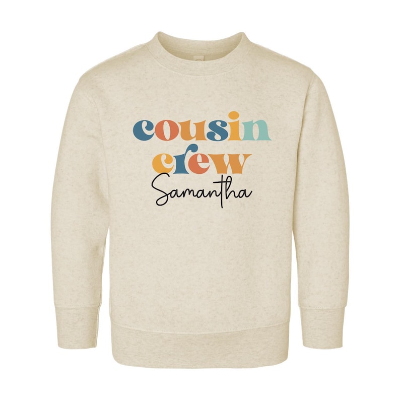 May include: A beige sweatshirt with the text "cousin crew Samantha" in colorful retro-style lettering.