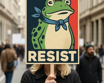 May include: A poster with a frog illustration wearing a blue scarf, set against a red and navy background. The word "RESIST" is printed in bold, cream-colored letters. The poster is held up in a crowd.