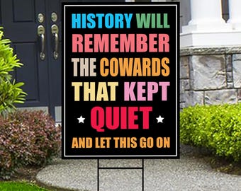May include: Black and white yard sign with colorful text that reads "HISTORY WILL REMEMBER THE COWARDS THAT KEPT *QUIET* AND LET THIS GO ON".