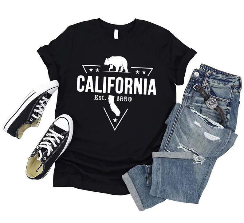 May include: Black t-shirt with a white graphic of a bear and a triangle with the text "CALIFORNIA Est. 1850" inside. The graphic also includes a star and the outline of the state of California.
