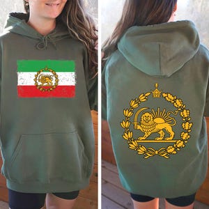 May include: Olive green hoodie featuring the Iranian flag on the front, with green, white, and red stripes and a golden emblem. The back displays a golden lion and sun emblem within a laurel wreath. The hoodie has a drawstring hood and a front pocket.