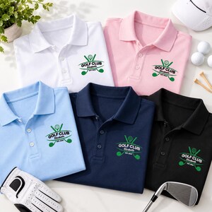 May include: Five polo shirts in white, pink, light blue, navy, and black, each featuring an embroidered green golf club logo with the text GOLF CLUB, Elizabeth, and EST. 2026. A white golf glove and a metal golf club head are also visible.
