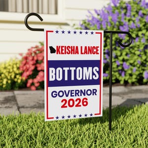 May include: A rectangular garden flag with a red and white border, featuring the text "Keisha Lance Bottoms Governor 2026" in white and red. The flag is displayed on a black metal stand in a grassy yard.