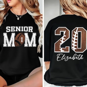 May include: Black sweatshirt with the text "SENIOR MOM" and a football graphic. The back of the shirt features the number "20" with a football design and the name "Elizabeth".