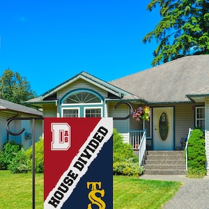 K&ouml;nnte beinhalten: Eine rot-blaue Gartenflagge mit dem Text "House Divided" und den Buchstaben "D.A.S." und "T.S." in Wei&szlig; und Gold. Die Flagge ist an einer schwarzen Metallstange befestigt.