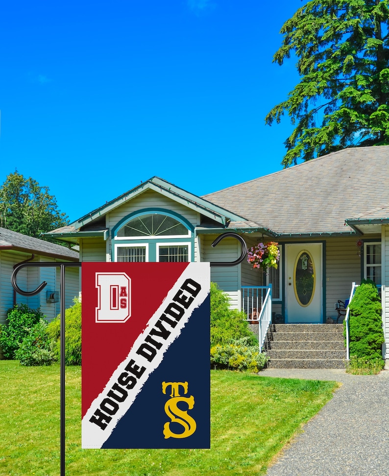 K&ouml;nnte beinhalten: Eine rot-blaue Gartenflagge mit dem Text "House Divided" und den Buchstaben "D.A.S." und "T.S." in Wei&szlig; und Gold. Die Flagge ist an einer schwarzen Metallstange befestigt.