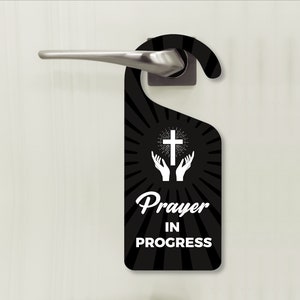 May include: Black door hanger with a white cross and hands raised in prayer. The text reads "Prayer in Progress".