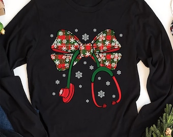 May include: Black long-sleeved top with a Christmas-themed design. The design features a plaid bow in red, green, and white, and a red and green stethoscope. Snowflakes are scattered around the bow and stethoscope.