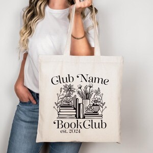 Puede incluir: Una bolsa de tela blanca con texto negro y un gr&aacute;fico de libros y flores. El texto dice "Club Name Book Club est. 2024".