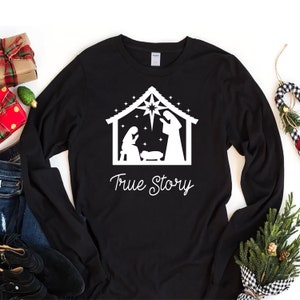 May include: Black long-sleeve shirt with a white silhouette of the nativity scene and the text "True Story".