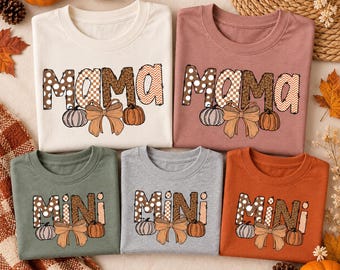 May include: Five t-shirts in cream, mauve, olive green, gray, and burnt orange. The top two shirts feature the text MAMA, and the bottom three feature MINI. Each letter has a patterned fill, accompanied by a bow and pumpkin graphic.