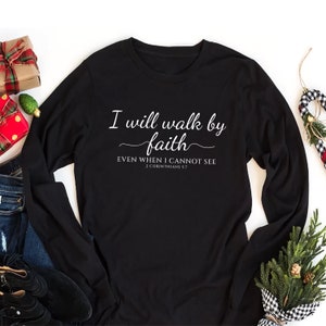 May include: Black long-sleeve shirt with white text that reads "I will walk by faith EVEN WHEN I CANNOT SEE 2 CORINTHIANS 5:7".