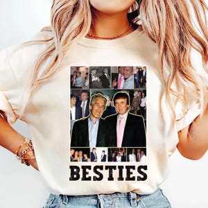 May include: Cream-colored t-shirt featuring a collage of images and the word "BESTIES" in bold, black letters. The collage includes multiple photos of two men in suits and ties. The shirt is made of a soft material.