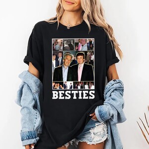 May include: Black t-shirt featuring a collage of images and the word "BESTIES" in white block letters. The collage includes images of two men in suits. The shirt is worn by a person wearing a denim jacket.
