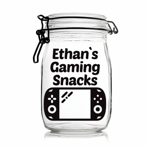 Peut inclure: Un pot en verre transparent avec un couvercle noir et une &eacute;tiquette noire sur laquelle est inscrit "Ethan's Gaming Snacks". L'&eacute;tiquette pr&eacute;sente &eacute;galement une illustration noir et blanc d'une manette de jeu vid&eacute;o.