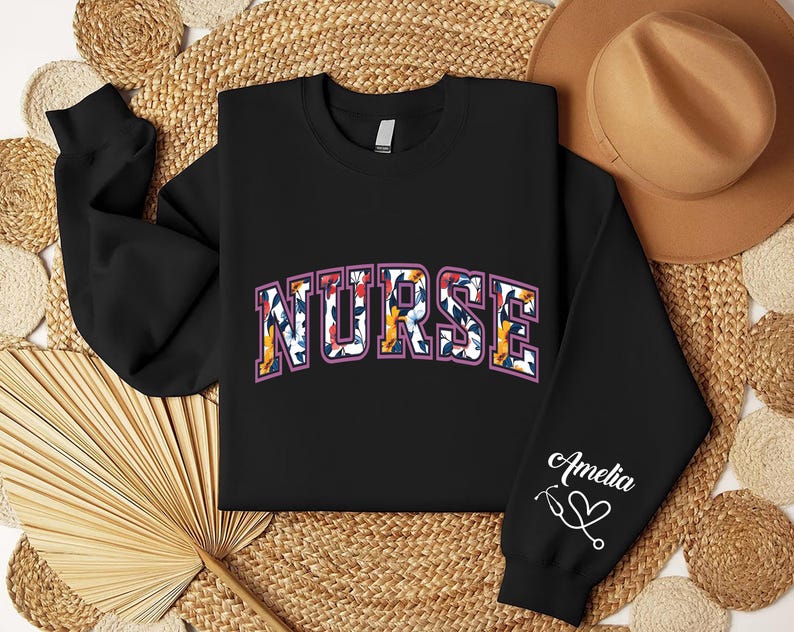 May include: Black sweatshirt with a floral print "NURSE" design and the name "Amelia" with a stethoscope and heart on the sleeve.