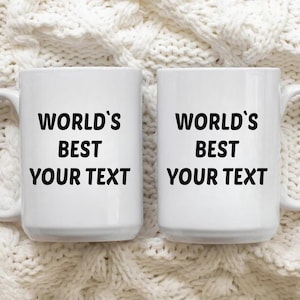 May include: Two white ceramic mugs with black text that reads "World's Best Your Text". The mugs are on a white knitted surface.