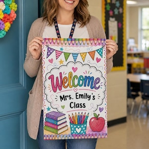 May include: A rectangular classroom sign featuring a white background with a colourful pencil border, a bunting banner, and the text "Welcome Mrs. Emily's Class". The design includes a stack of four books, a pencil holder, and a red apple illustration.