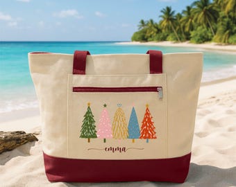 May include: A beige canvas tote bag with dark red handles and a matching dark red base. The front features a zippered pocket with a graphic of five stylized Christmas trees in green, pink, gold, blue, and red, with the name Emma printed below.