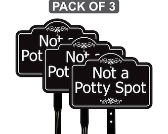 May include: Three black garden signs with white text that reads "Not a Potty Spot". The signs have a decorative top edge and are mounted on black stakes. The text "PACK OF 3" is at the top.