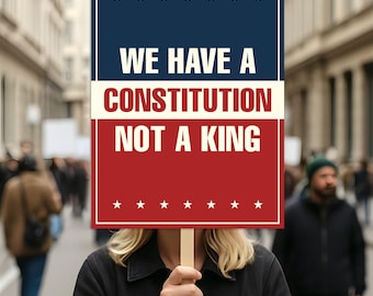 May include: A person holding a sign with the text "WE HAVE A CONSTITUTION NOT A KING". The sign has a blue top with white stars, a cream middle, and a red bottom with white stars. The background shows a crowd of people.