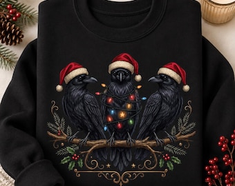 Puede incluir: Una sudadera negra de cuello redondo con un gráfico de tres cuervos negros posados en una rama. Cada cuervo lleva un gorro de Papá Noel rojo y blanco. El cuervo central está envuelto en luces navideñas de colores. Hojas de acebo y bayas rojas.