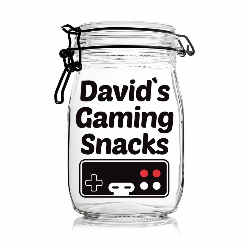 Peut inclure: Un pot en verre transparent avec un couvercle noir et une &eacute;tiquette noire qui dit "David's Gaming Snacks". L'&eacute;tiquette comporte &eacute;galement une image noir et blanc d'une manette de jeu vid&eacute;o avec des boutons rouges.