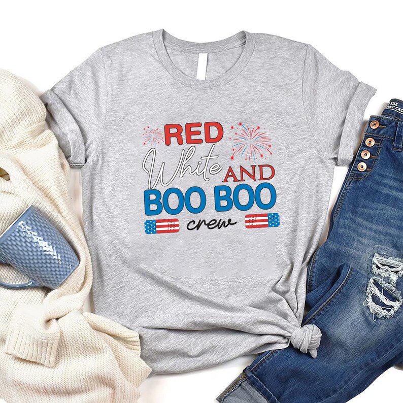 May include: Gray t-shirt with the text "Red White and Boo Boo Crew" in red, white, and blue. The text is surrounded by fireworks and American flag graphics.