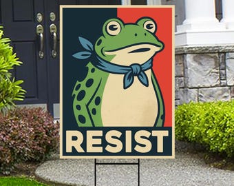 May include: A garden sign with a cartoon frog wearing a blue neckerchief, set against a red and navy blue backdrop. The word "RESIST" is printed in bold white letters at the bottom of the sign.