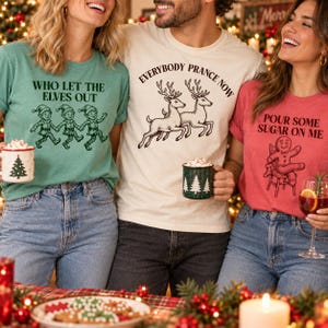 Puede incluir: Tres camisetas con gráficos navideños: una verde con elfos y el texto 'WHO LET THE ELVES OUT', una crema con renos y 'EVERYBODY PRANCE NOW', y una roja con un hombre de jengibre y 'POUR SOME SUGAR ON ME'.