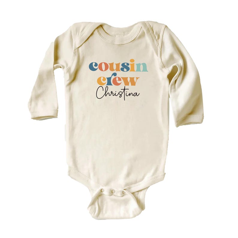 May include: A cream colored long-sleeved baby onesie with the text "cousin crew Christina" in colorful retro font.