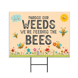 May include: A yellow and black bee themed garden sign with the text "Pardon our weeds we're feeding the bees". The sign has a cartoon sun, cloud, and bees on a beige background with a green grass border.